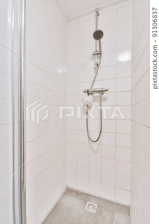 Shower faucets attached to tiled wall near glass partition and ornamental curtail in washroom at home 91306837