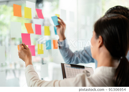 Two business executive team holding and taking notes keyword on board wall to brainstorm about a new business project for planning marketing plan together in the office 91306954