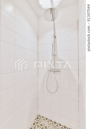 Shower faucets attached to tiled wall near glass partition and ornamental curtail in washroom at home 91307044