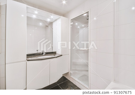 Tiled shower cabin with glass door located near sink and mirror in light restroom in contemporary apartment 91307675