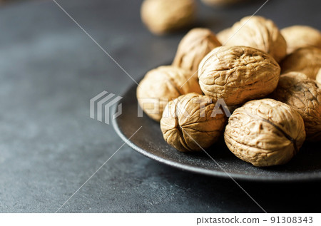 Walnuts in a plate on a dark concrete background. Nuts are a source of vegetable protein and vitamins. Copy space, selective focus 91308343