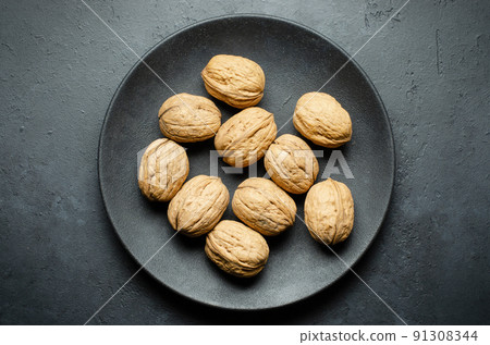 Walnuts in a plate on a dark concrete background. Nuts are a source of vegetable protein and vitamins. Flat top view, copy space. 91308344