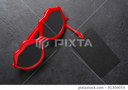 Red sunglasses. Black tag. Dark concrete background. The concept of the holiday sales on black Friday. Copy space. Red sunglasses. Black tag. Dark concrete background. The concept of the holiday sales on black Friday. Copy space. 91309059