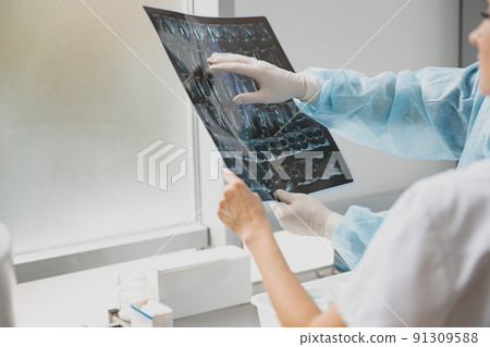 Close up of two doctors in uniform look and discuss an X-ray or MRI scan of the patient spine Close up of two doctors in uniform look and discuss an X-ray or MRI scan of the patient spine 91309588