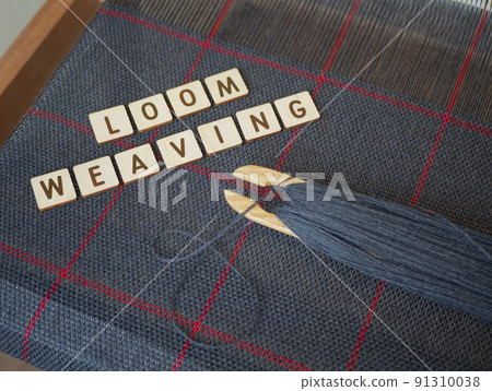 Making cloth in the traditional way. Woven blue fabric with red stripes. Concept of loom weaving, cloth art and craft. Weaving loom, wooden shuttle and handwoven scarf 91310038