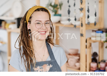 Happy young female clerk or owner of small earthenware shop looking at camera Happy young female clerk or owner of small earthenware shop looking at camera 91310702