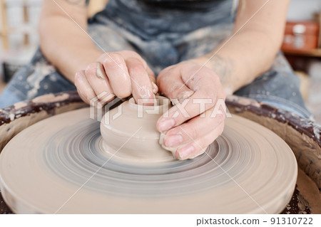 Hands of young female potter on raw clay item on rotating pottery wheel Hands of young female potter on raw clay item on rotating pottery wheel 91310722