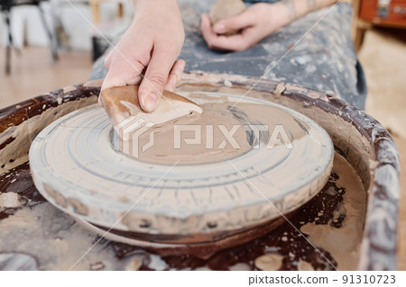 Hand of young creative female potter applying clay on rotating pottery wheel Hand of young creative female potter applying clay on rotating pottery wheel 91310723