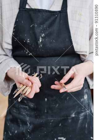 Hands of young female artisan in black apron holding group of handtools 91310890