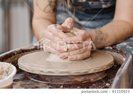 Hands of young creative female holding by rotating pottery wheel in workshop Hands of young creative female holding by rotating pottery wheel in workshop 91310925