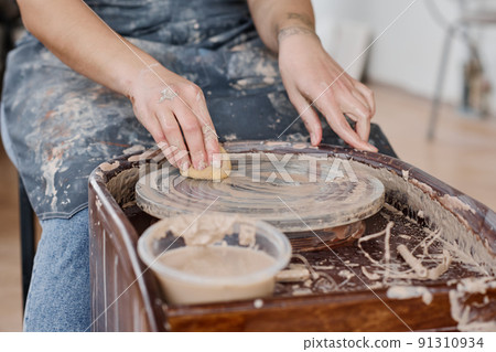 Hands of young woman wiping pottery wheel with wet sponge after work 91310934