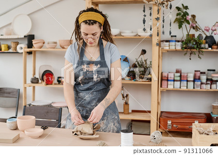 Young woman in workwear tying wrapped and packed earthenware item with thread Young woman in workwear tying wrapped and packed earthenware item with thread 91311066