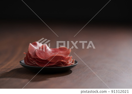 saucer with this slices of bresaola on walnut wood table saucer with this slices of bresaola on walnut wood table 91312021