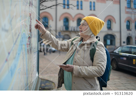 Happy 50s woman with backpack travelling looking at city map at urban street. Local travel. 91313620