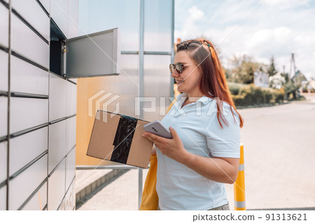 Young caucasian woman getting parcel from cell of automatic post terminal outdoors. Young caucasian woman getting parcel from cell of automatic post terminal outdoors. 91313621
