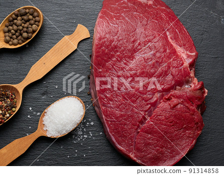 Raw beef tenderloin lies on a wooden cutting board on a black table, top view Raw beef tenderloin lies on a wooden cutting board on a black table, top view 91314858