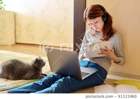 Preteen girl studying at home using laptop along with cat 91315960