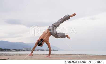 Shirtless caucasian man doing acrobatic wheel on the beach.  91321879