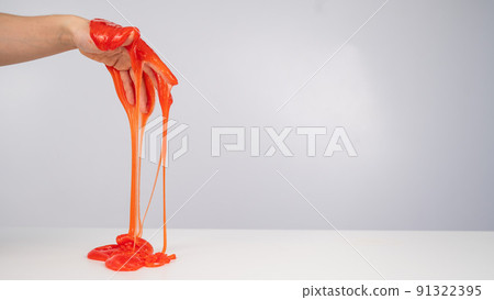 Red slime flowing down from a woman's hand on a white background. Red slime flowing down from a woman's hand on a white background. 91322395