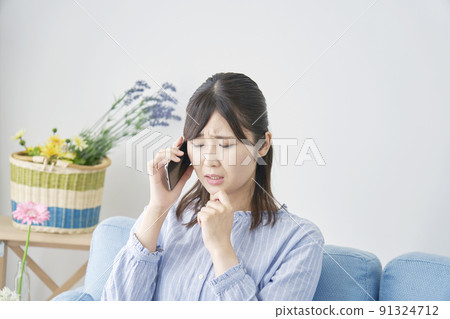 A woman in trouble while calling on her smartphone in the living room A woman in trouble while calling on her smartphone in the living room 91324712