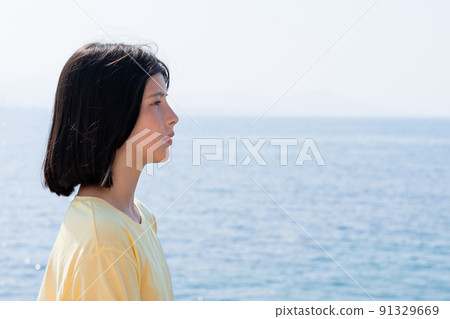 A young girl stands by the sea and looks into the distance. 91329669