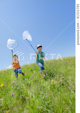 Brothers catching insects on a hill where wild flowers bloom 91331785