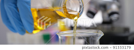 A hand in a glove pours a yellow liquid in the laboratory A hand in a glove pours a yellow liquid in the laboratory 91333179