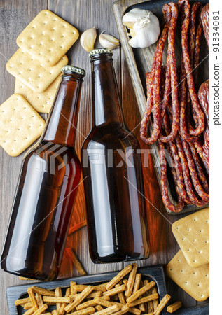 Beer in dark glass bottles, salty snacks for beer, sausage. Brown wooden background. Drinks and food for a drunken party Beer in dark glass bottles, salty snacks for beer, sausage. Brown wooden background. Drinks and food for a drunken party 91334081