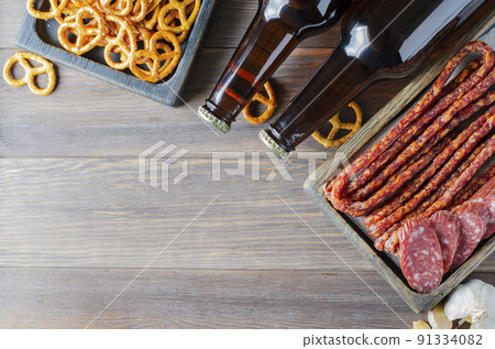Beer in dark glass bottles, salty snacks for beer, sausage. Brown wooden background. Drinks and food for a drunken party. Copy space. Beer in dark glass bottles, salty snacks for beer, sausage. Brown wooden background. Drinks and food for a drunken party. Copy space. 91334082