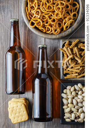 Beer in glass bottles and salty snacks for beer in wooden dishes. Rustic style. Brown wooden background. Beer in glass bottles and salty snacks for beer in wooden dishes. Rustic style. Brown wooden background. 91334096