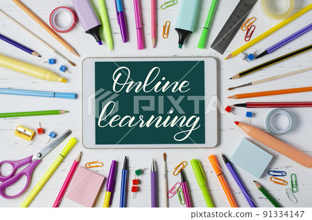 Online learning - handwritten inscription on a tablet. The concept of distance training for children. Tablet and office supplies on a white wooden background. Online learning - handwritten inscription on a tablet. The concept of distance training for children. Tablet and office supplies on a white wooden background. 91334147