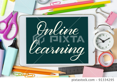 Online learning - handwritten inscription on a tablet. The concept of distance training for children. Tablet and office supplies on a white wooden background. 91334295