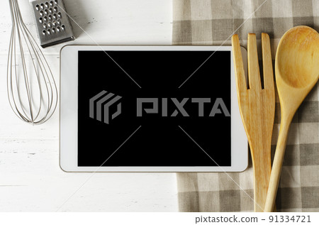 A tablet computer and cooking battery on a white background. Copy space. Concept of cooking recipes A tablet computer and cooking battery on a white background. Copy space. Concept of cooking recipes 91334721