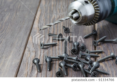 Metal screws and an electric drill on a wooden background. Tool for fixing and repairing. Copy space Metal screws and an electric drill on a wooden background. Tool for fixing and repairing. Copy space 91334766