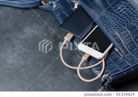 Blue Power Bank and telephone in the women's bag. Dark grey concrete background. Copy space Blue Power Bank and telephone in the women's bag. Dark grey concrete background. Copy space 91334924