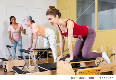 Female instructor helps women perform an exercise on a combined chair Female instructor helps women perform an exercise on a combined chair 91334967