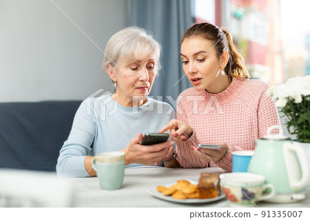 Girl showing pictures on smartphone to interested elderly mother Girl showing pictures on smartphone to interested elderly mother 91335007