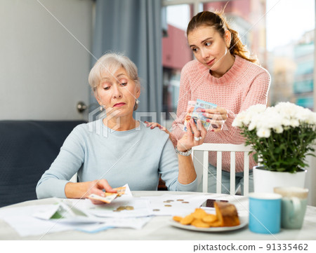 Young woman receiving money from her senior mother Young woman receiving money from her senior mother 91335462