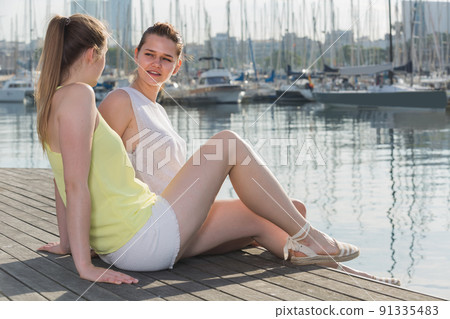 Portrait of young traveling girls sitting on promenade sea 91335483