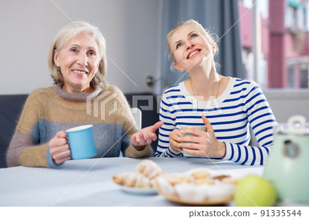 Mature mother and her adult daughter drink tea and chat 91335544