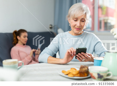 Young woman and her grandmother with smartphones at home Young woman and her grandmother with smartphones at home 91335606