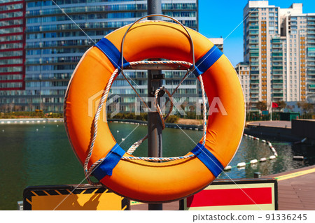 Orange lifebuoy hanging on a pillar near water in residential complex 91336245