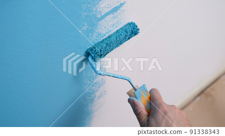 Hand holds roller and paints wall blue closeup Hand holds roller and paints wall blue closeup 91338343