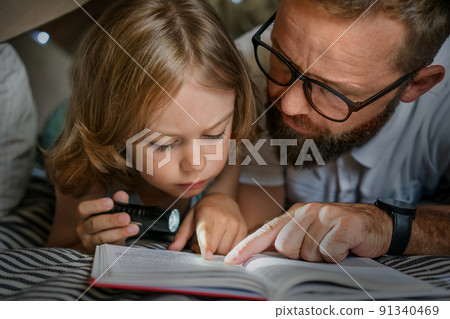 Father and son playing and reading in a kid tent at home. Father and son playing and reading in a kid tent at home. 91340469