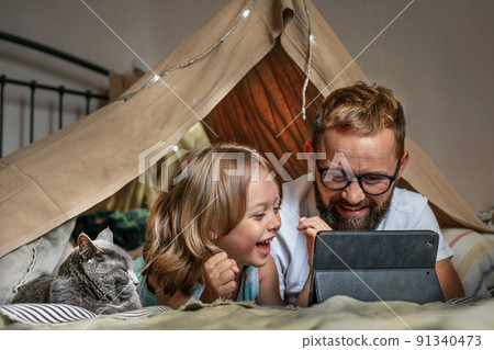 Father and son playing in a teepee tent at home. Father and son playing in a teepee tent at home. 91340473