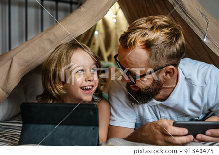 Father and son playing in a teepee tent at home. Father and son playing in a teepee tent at home. 91340475