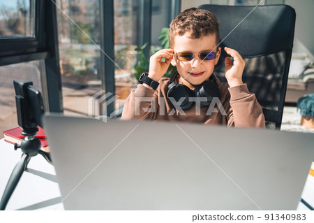 Boy puts on glasses while sitting at laptop Boy puts on glasses while sitting at laptop 91340983