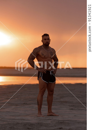 Handsome young muscular italian man posing shirtless on the beach, sunset summer time 91341921