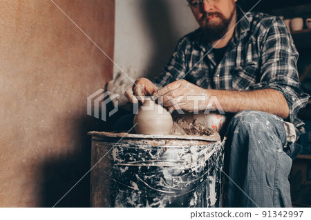 Pottery master works on pottery wheel in workshop. 91342997