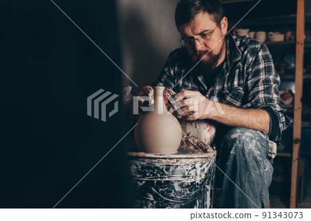Master works on the potter's wheel creating a jug of clay. 91343073